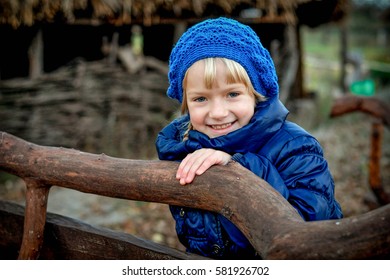 little blonde child girl smile holding wooden branch at park. wearing a blue coat and hat
