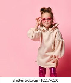 Little blonde girl in glasses, stylish hoodie and leggings. Looking at you intently or scared, posing on pink studio background. Childhood, sincere emotions, fashion, advertising. Close up, copy space - Shutterstock ID 1811770102