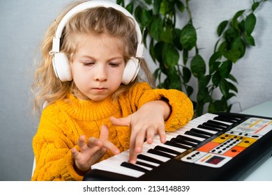 a little blonde girl in headphones smiling and playing the synthesizer, the concept of teaching children music.