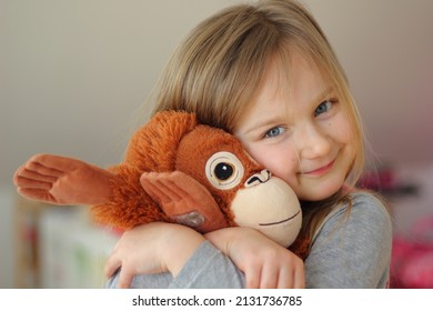 Little blonde Girl hugs her favorite toy. This is a big orangutan soft toy. Love and tenderness. Happy childhood concept. High-quality photo. A gift for a birthday or other holiday.