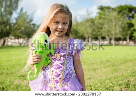 Little blonde girl with long hair cosplaying Rapunzel with an chameleon Pascal. Blonde little girl in a purple dress. Halloween costume, Halloween party dress up