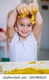 Little blonde girl play with yellow magic sand on white glowing table. Sensory development. Lessons in kindergarten. Sensorics