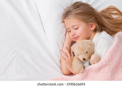 little blonde girl sleeping in bed hugging a teddy bear under a pink knitted blanket, space for text - Powered by Shutterstock