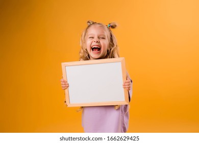 little blonde girl smiling and holding an empty drawing Board, space for text,isolate on a yellow background - Powered by Shutterstock