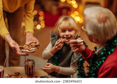 Little blonde girl smiling while eating cookies with her grandparents during a Christmas family hangout - Powered by Shutterstock