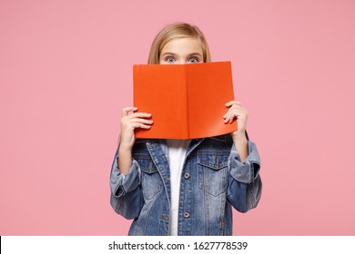 Little blonde kid girl 12-13 years old in denim jacket posing isolated on pastel pink background children portrait. Childhood lifestyle concept. Mock up copy space. Covering face with book, notebook