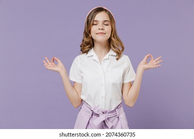 Little Blonde Kid Girl 12-13 Years Old In White Shirt Hold Hands In Yoga Om Aum Gesture Relax Meditate Try Calm Down Isolated On Purple Background Children Studio Portrait. Childhood Lifestyle Concept