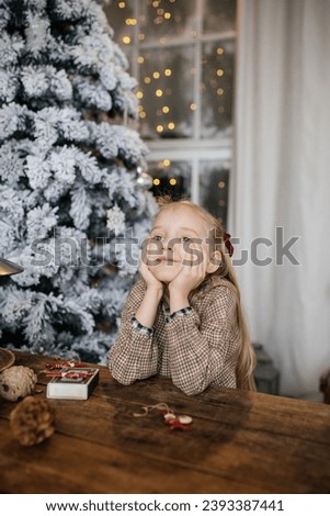 Little blondhaired girl in the decorated room with christmas trees on her background is dreaming and  waiting for Christmas 