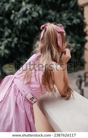 Little blondhaired girl with a dusty pink bow standing on the Mediterranean terrace looking somewhere in the distance 