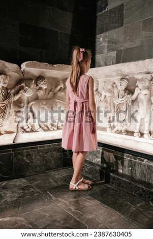 Little blondhaired girl watching at ancient barelief in Archeological museum of Antalya 