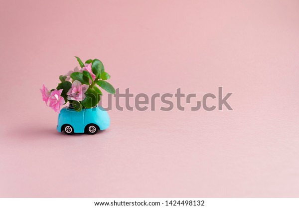 little blue toy car with a bouquet of flowers on a\
pink background. Valentine\'s day. Flower delivery. 8 March,\
International Happy Women\'s Day.for a declaration of love. soft\
focus, copy space