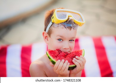 Little Blue-eyed Blond Boy Wearing Yellow Diving Goggles Eating Watermelon Sitting On The Striped Red And White Beach Towel In The Summer