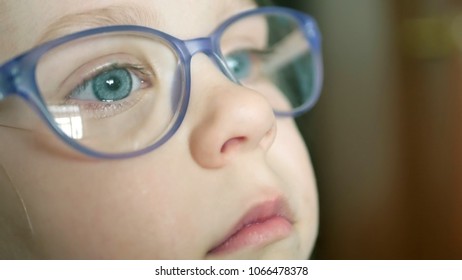 A little blue-eyed girl with blond hair in glasses looks at something