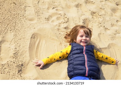 Little Boy, 3 Years Old, Lies In The Sand On The Beach And Makes A 