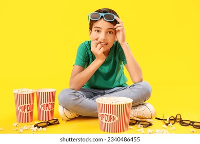 Little boy in 3D glasses with popcorn biting nails on yellow background