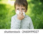 A little boy 4 years old blows his nose into a paper napkin against a background of greenery. Spring exacerbation of allergy to poplar fluff. Allergies in children hay fever