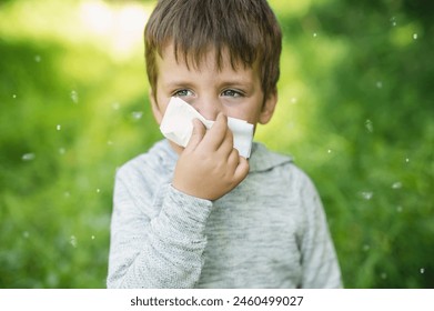 A little boy 4 years old blows his nose into a paper napkin against a background of greenery. Spring exacerbation of allergy to poplar fluff. Allergies in children hay fever - Powered by Shutterstock