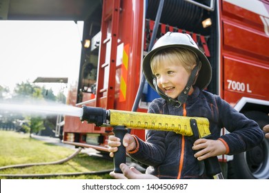 Little Boy Acting Like A Fireman Holding Firehose Nozzle And Splashing Water.