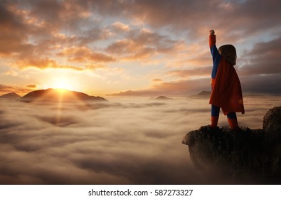 Little boy acting like a superhero on top of the mountain at sunset with copy space