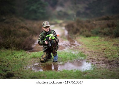 A little boy with ADHD, Autism poses in camouflage (DPMs) with his BB gun, rifle outdoors playing in the wild, Asperger syndrome