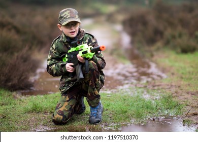 A little boy with ADHD, Autism poses in camouflage (DPMs) with his BB gun, rifle outdoors playing in the wild, Asperger syndrome