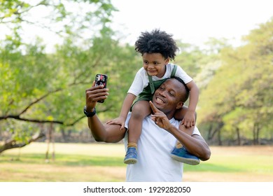 Little boy african american is sitting on his father and selfie. Smiling happy father and son having picnic in park.