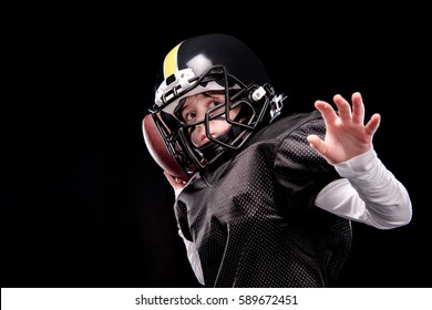 Little Boy American Football Player In Uniform Throwing Ball Isolated On Black