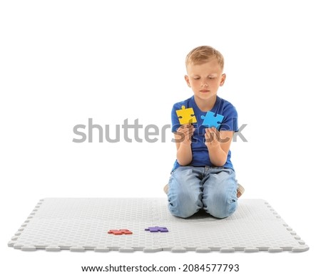 Little boy with autistic disorder doing puzzle on white background