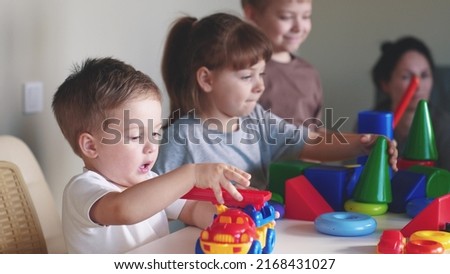 little boy and baby girl play in kindergarten. a group of children play toys cubes and cars on the table in kindergarten. happy family preschool education concept. indoor nursery baby toddler home