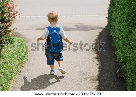 Little boy with backpack walking along road