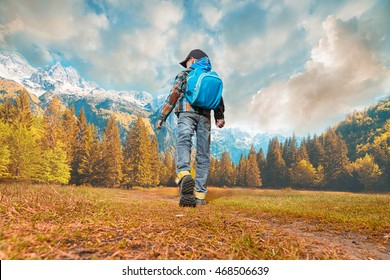Little boy with backpack walking in nature. Autumn time, cloudy sky and snowly peak of mountains