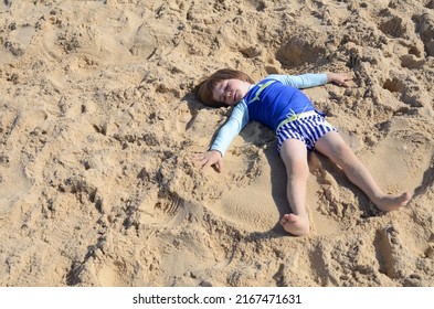 A Little Boy In A Bathing Suit Lies On The Sand, Plays 