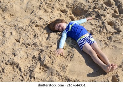 A Little Boy In A Bathing Suit Lies On The Sand, Plays 