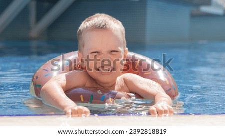 Little boy bathing in swimming pool with lifebuoy donut, smiling and happy