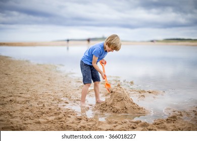 A little boy is at the beach building a sand castle. - Powered by Shutterstock