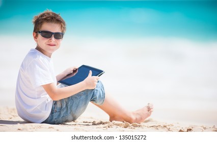 Little Boy At Beach Playing On A Tablet Device
