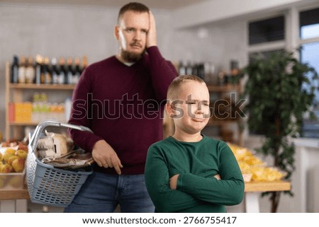 Little boy behaving capricious while his father looking discontentedly in grocery store