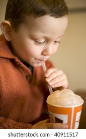 Little Boy Blowing Bubbles Through A Straw Into In His Milkshake