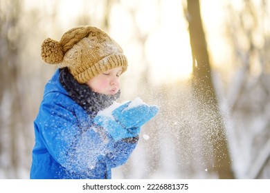 Little boy blowing snow from his hands. Child enjoy walking in the park on snowy day. Baby having fun during snowfall. Outdoor winter activities for family with kids. - Shutterstock ID 2226881375