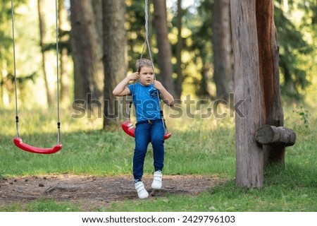 A little boy in blue clothes sits on a entwined rope swings in the forest.