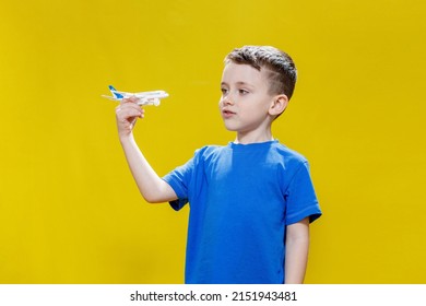 Little boy in a blue T-shirt holds a toy white plane and plays on a yellow background. Copy space. Travel concept.