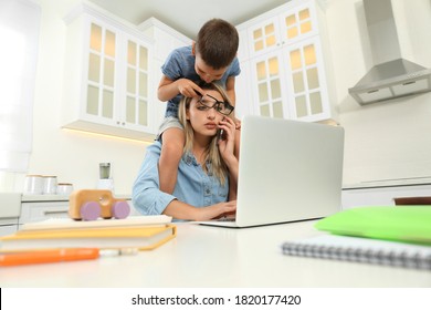 Little boy bothering mother at work in kitchen. Home office concept