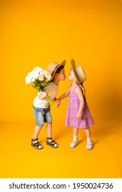 a little boy with a bouquet of flowers kisses a little girl in a straw hat on a yellow background with space for text