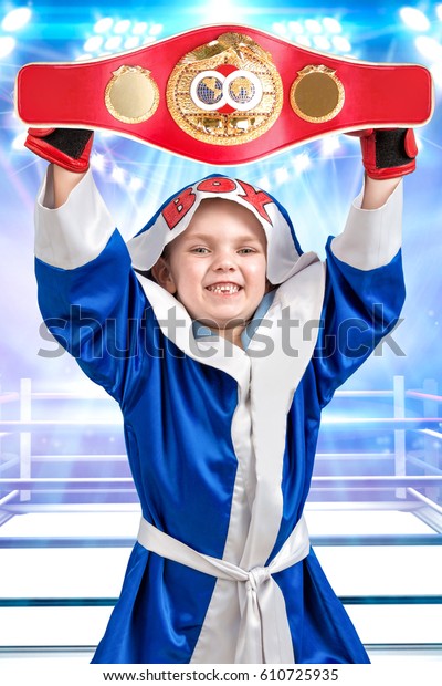 Little boy\
boxer holding Boxing championship belt.The athlete in scrubs in the\
background of the ring.Little\
champion.