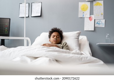 Little Boy Breathing With Oxygen Tube In His Nose While Sleeping In Bed And Holding Treatment At Hospital