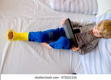 Little Boy With Broken Leg Playing On Tablet