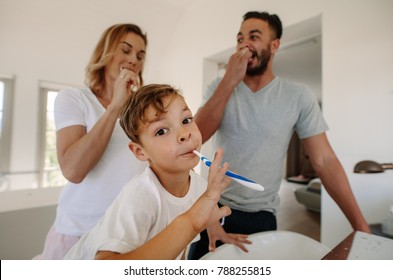 Little Boy Brushing Teeth With His Parents In Bathroom. Family Brushing Teeth Together In Bathroom.