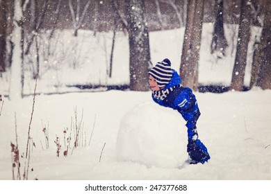 Little Boy Building Snowman In Winter Park