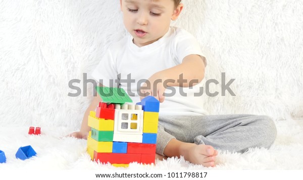 Little boy,\
builds a toy house of colored blocks, sitting on a white\
background, close-up. Child and toys -\
2
