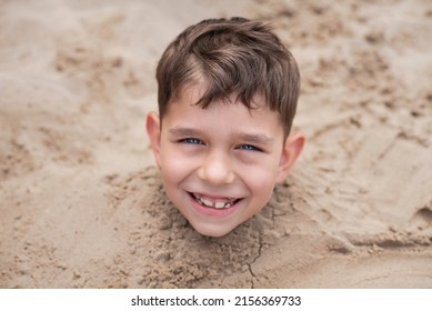 The little boy is buried in the sand, only his head is visible over the sand, the boy is happy and smiling, happy to rest at sea in summer. The concept of family vacation at sea 